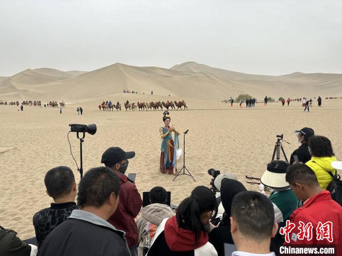 圖為2023年4月底，敦煌大漠“逐舞者”奧楠在鳴沙山月牙泉景區(qū)視頻直播，吸引游人圍觀。　馮志軍 攝